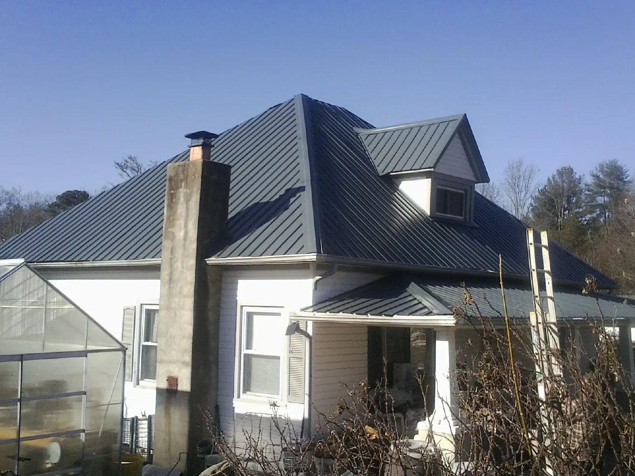 Dark blue standing seam metal roof on a white farmhouse with dormer — Slate & Tile Roof Repair by Roofing Brothers in Bakersville