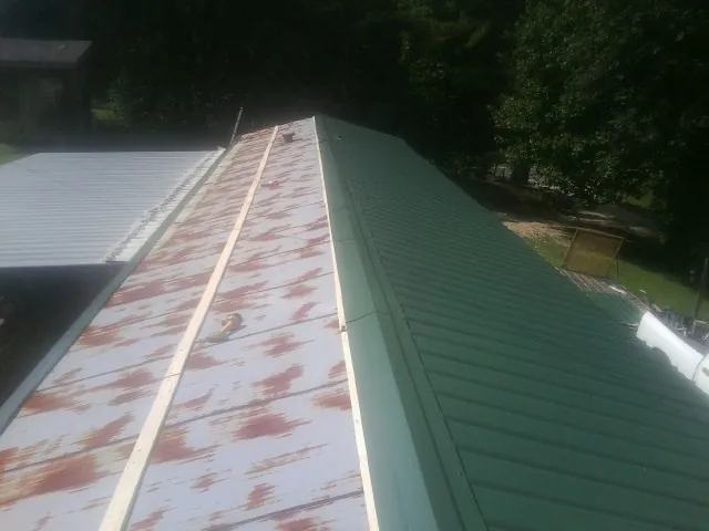 Old rusted panels beside newly installed green metal roofing — Wind Damage Roof Repair by Roofing Brothers in Bakersville