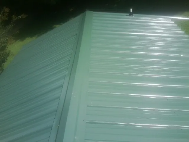 New green metal panels meeting at the ridge of a roof — Flat Roof Repair work by our crew in Bakersville