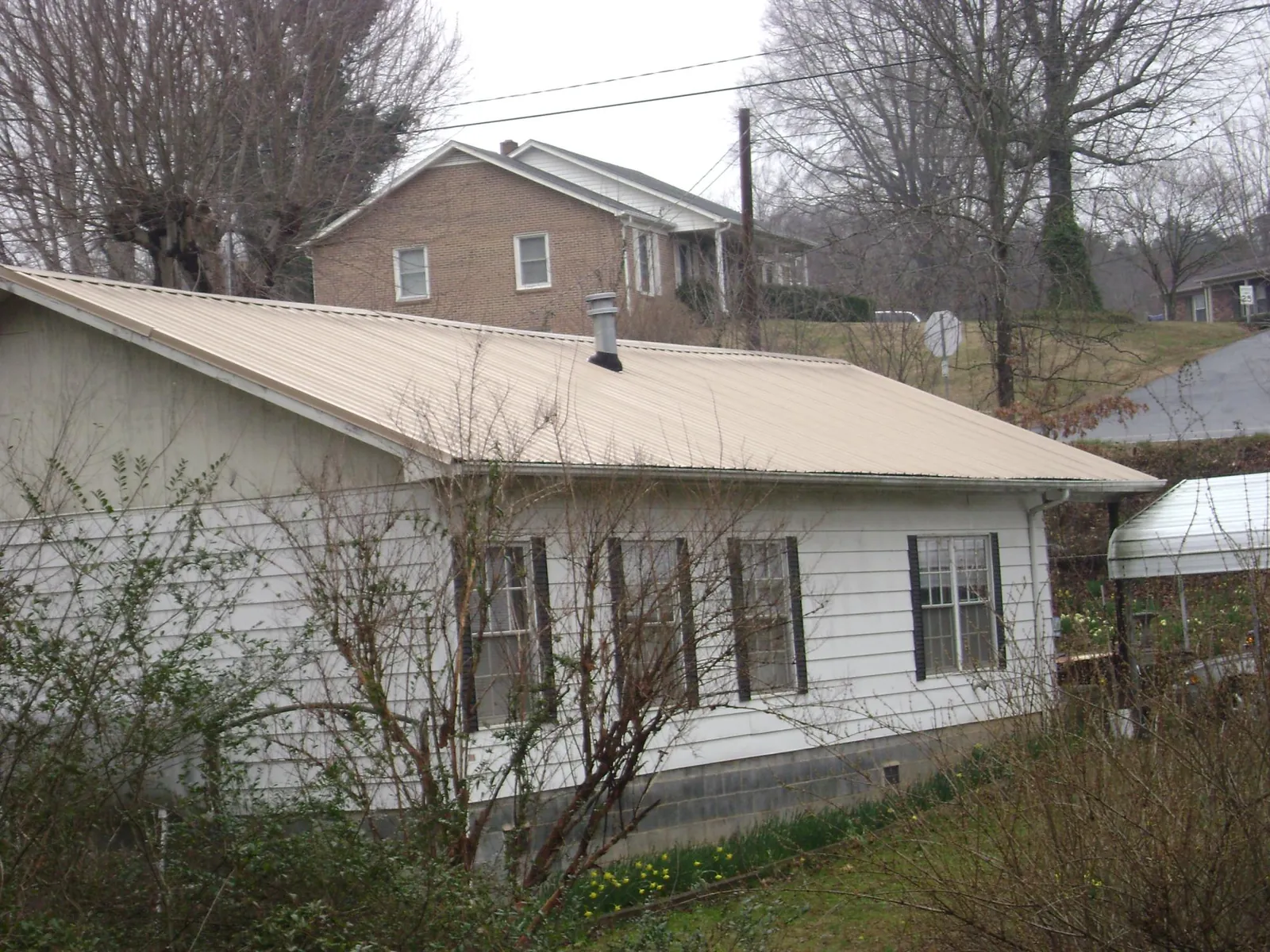 Tan metal roof on a white sided house set into a hillside — Commercial Roofing by Roofing Brothers in Bakersville