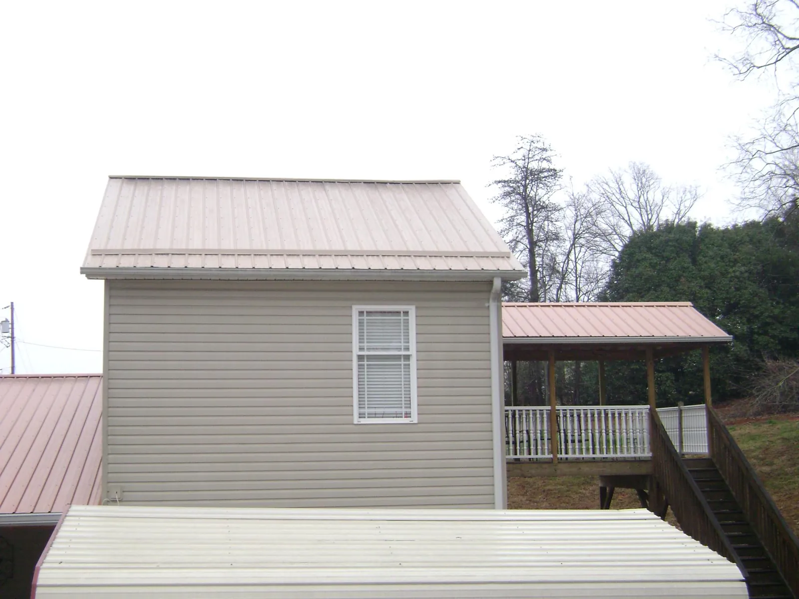Tan metal roofs on a two story addition and attached porch, from a Roof Replacement job in Bakersville